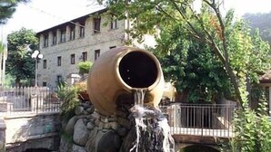 A large clay pot with water flowing from its opening, situated on a stone structure with a small bridge in the background. - Villaggio Albergo San Lorenzo e Santa Caterina (Pescia)