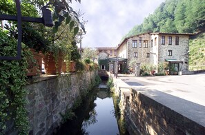 A stone building with a covered outdoor seating area and a narrow water channel. - Villaggio Albergo San Lorenzo e Santa Caterina (Pescia)