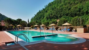 A swimming pool with multiple lounge chairs and umbrellas, surrounded by a forested hillside. - Villaggio Albergo San Lorenzo e Santa Caterina (Pescia)