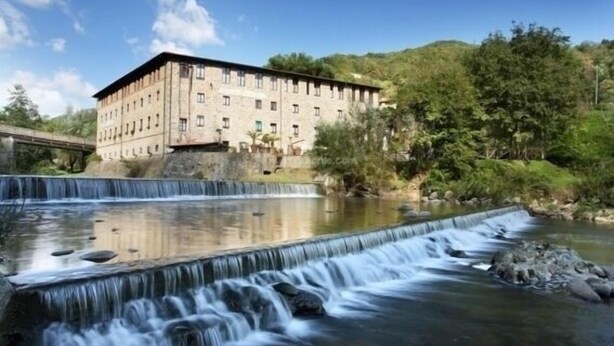 A building with a long, rectangular structure, a bridge in the background, and a waterfall in the foreground. - Villaggio Albergo San Lorenzo e Santa Caterina (Pescia)
