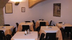 Un comedor con varias mesas cubiertas de manteles blancos, sillas negras y un cuadro en la pared.