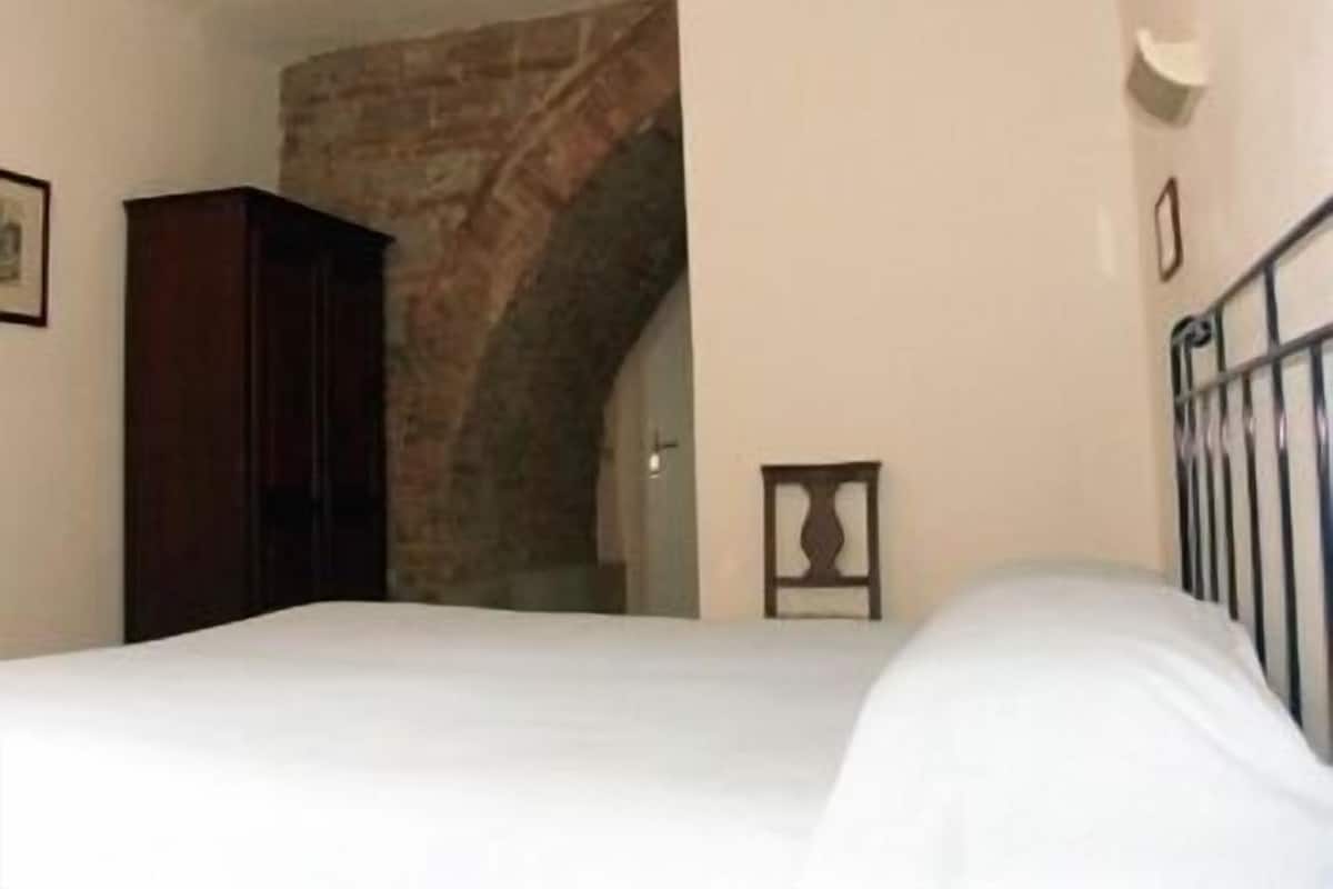 A bedroom with a bed, a wooden wardrobe, a brick wall, and a small picture frame on the wall.