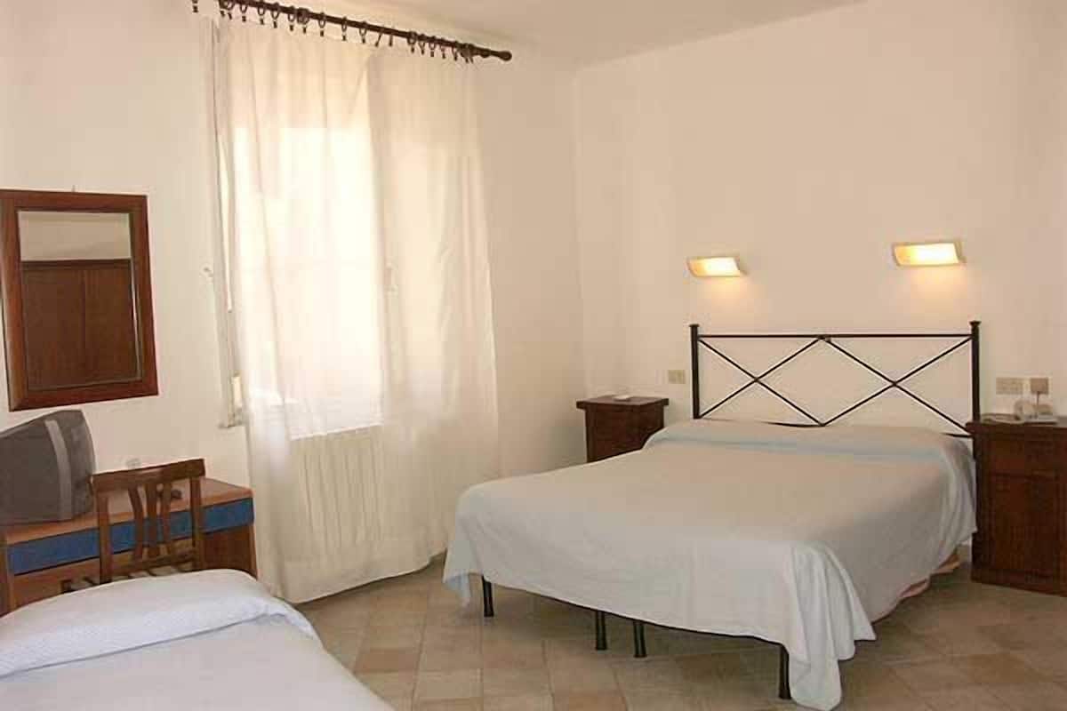 A bedroom with two beds, a wooden desk, a chair, a mirror, and two bedside lamps.