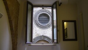 Una habitación con ventana que da a un muro de piedra, un radiador y un espejo enmarcados en la pared.