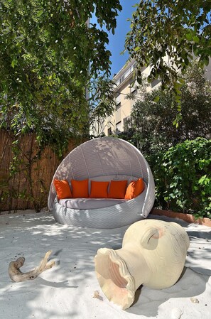 A round, woven outdoor seating area with orange cushions, a large decorative vase, and a bamboo fence in a sunny courtyard. - Villa Angelica (Venice)