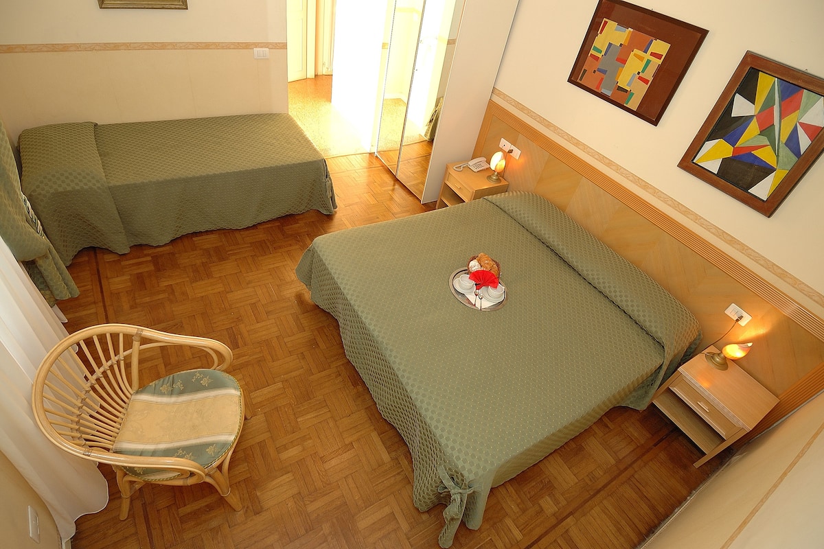 A room with two beds, a wooden floor, a chair, and artwork on the walls.