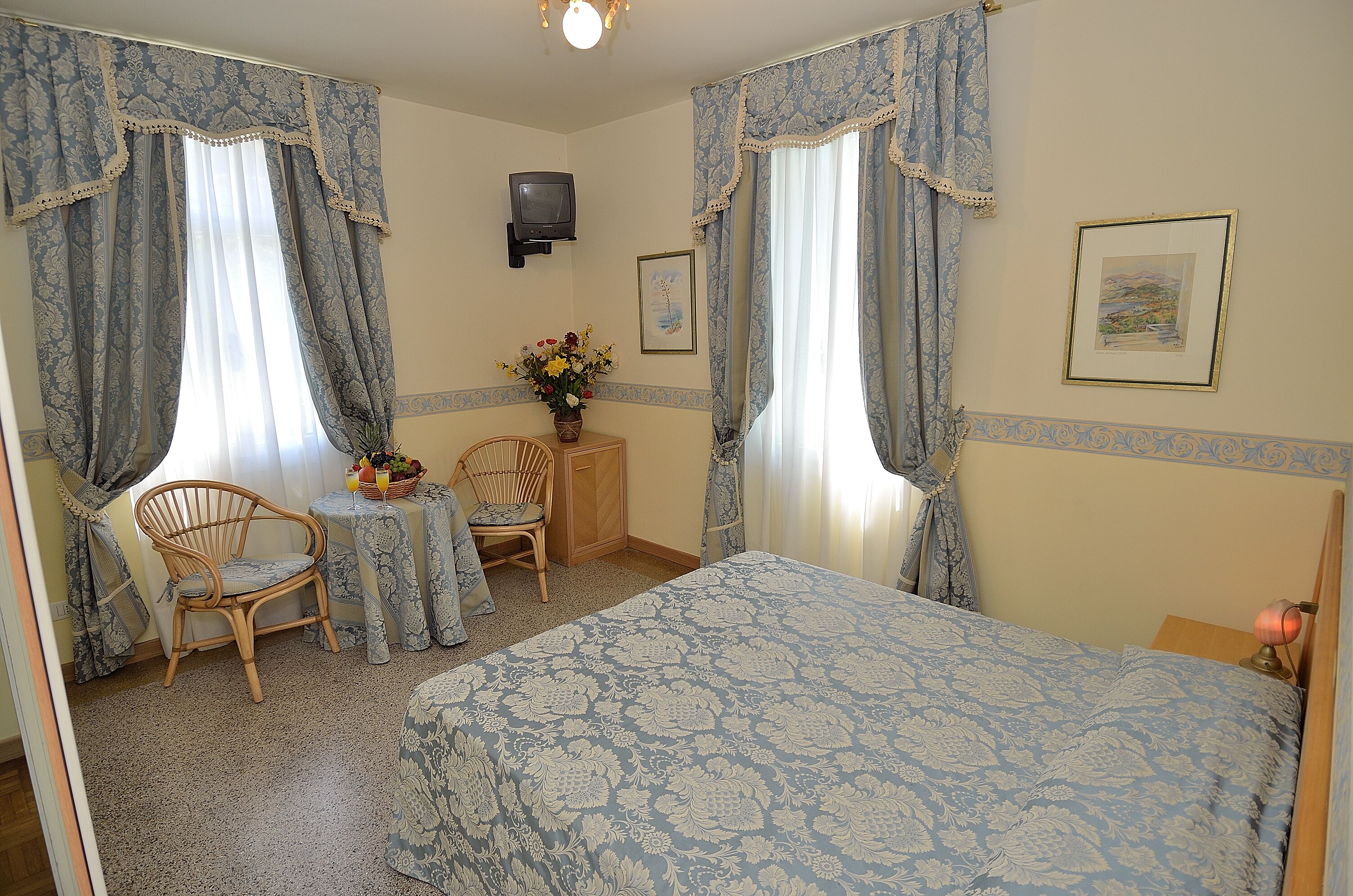 A bedroom with a bed, two chairs, a small table, a TV, and a framed picture on the wall.