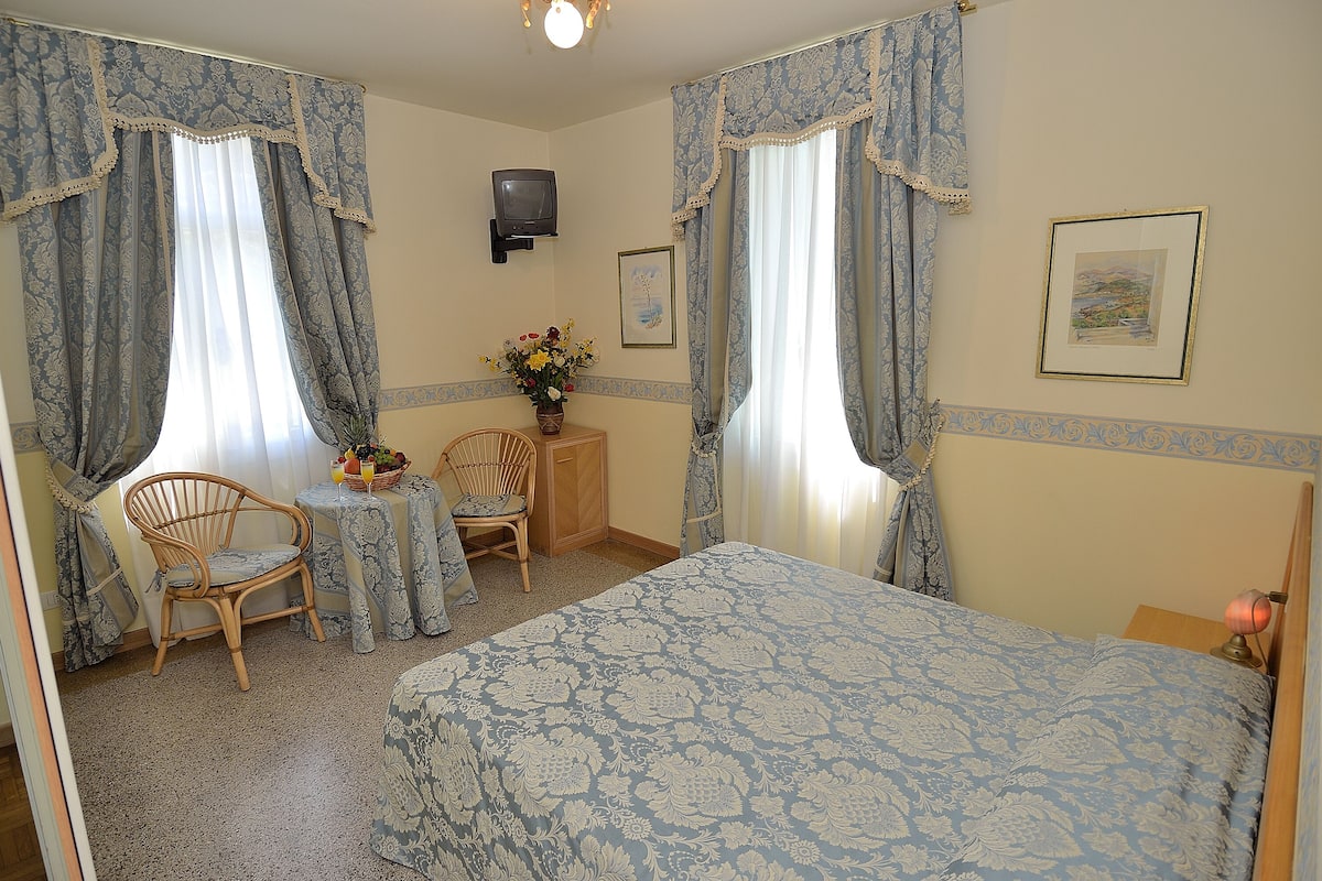A bedroom with a bed, two chairs, a small table, a TV, and a framed picture on the wall.