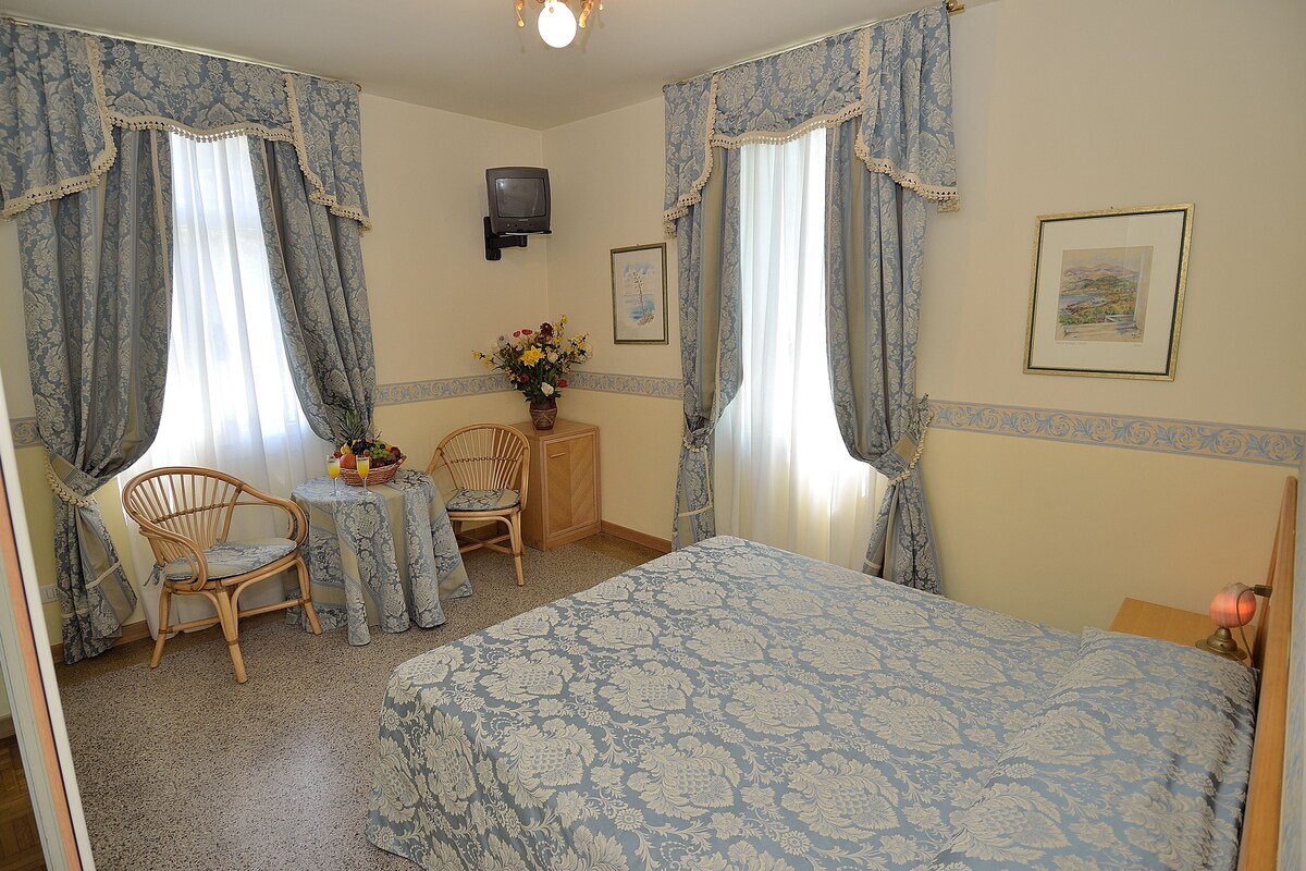 Ein Schlafzimmer mit einem Bett, zwei Stühlen, einem kleinen Tisch, einem Fernseher und einem gerahmten Bild an der Wand.