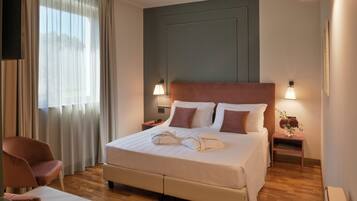 Una camera d'albergo con un letto grande, due lampade ai comodini, una sedia, un comodino e una finestra con tende.