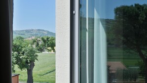 Vista por una ventana, cielo despejado, un árbol y una colina distante con edificios.
