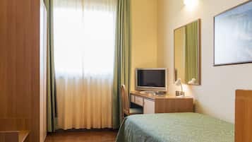 Une chambre d’hôtel avec une armoire en bois, un bureau avec un ordinateur, un lit recouvert d’une courtepointe verte, une fenêtre avec des rideaux et un miroir fixé au mur.