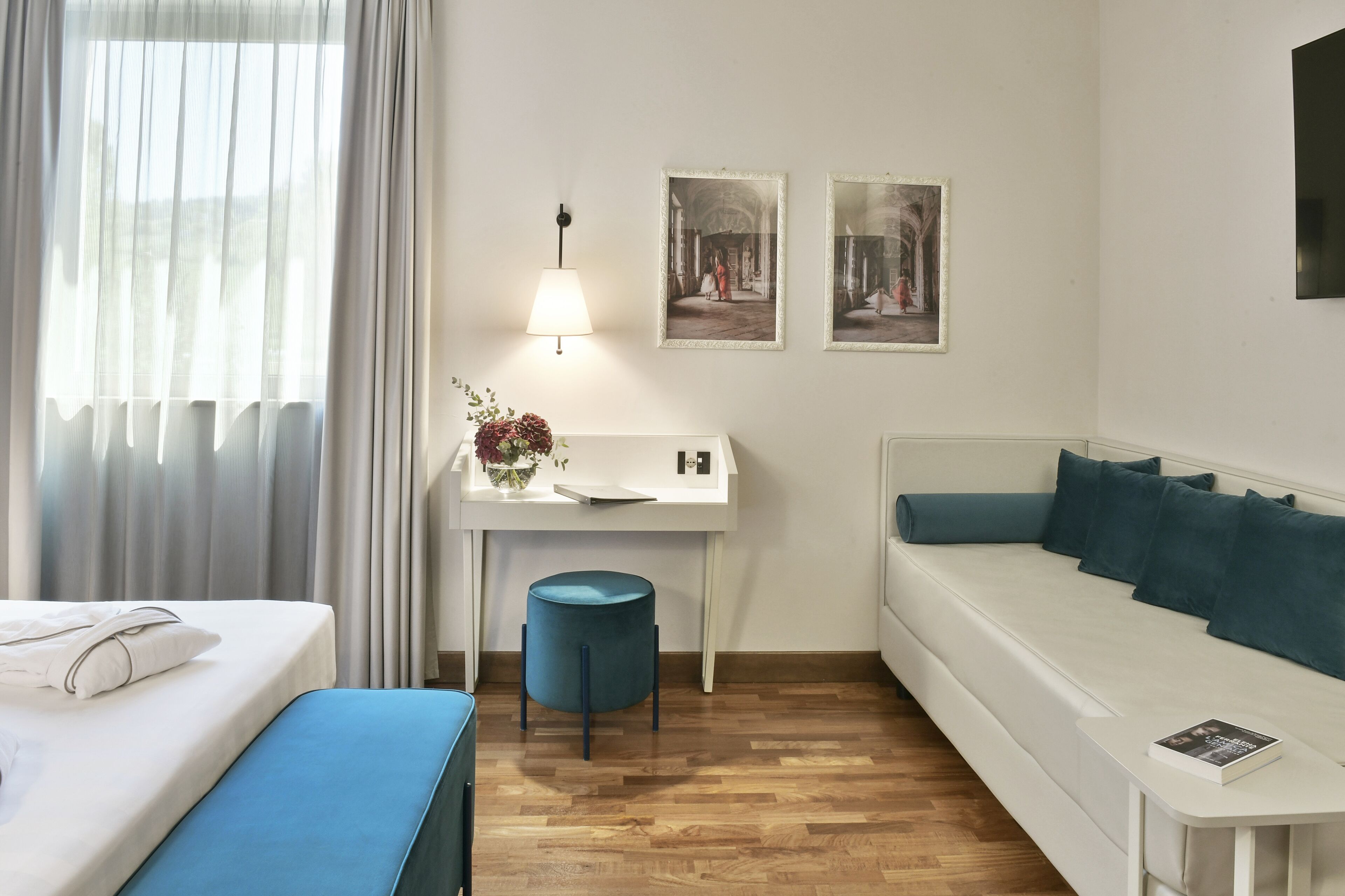 A hotel room with a bed, a desk with a lamp, a sofa, and two framed pictures on the wall.