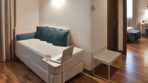 Una habitación de hotel moderna con cama, una laptop sobre una mesita de noche y un escritorio pequeño con una silla.