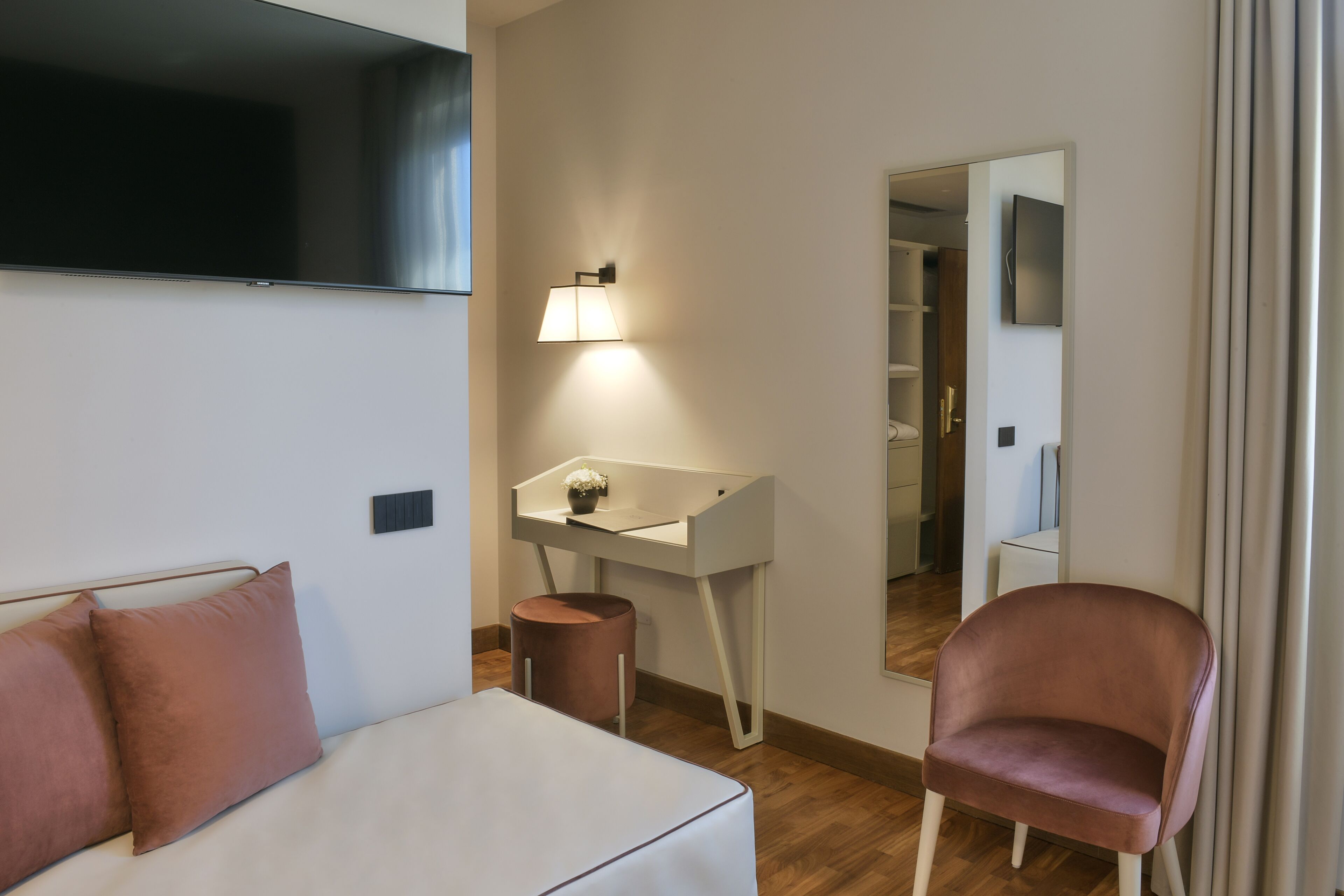 A hotel room with a bed, a desk with a lamp, a chair, and a mirror.