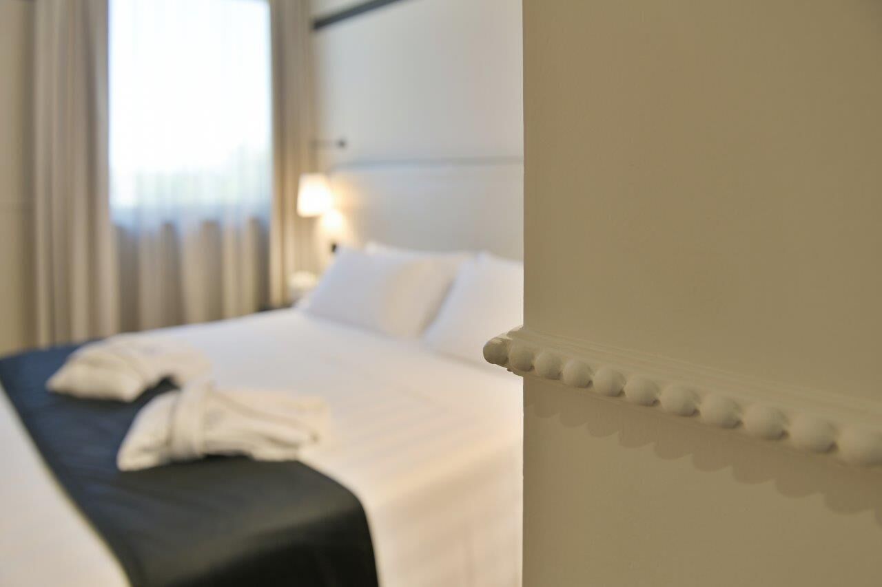 A hotel room with a neatly made bed, a bedside lamp, and a window with curtains.