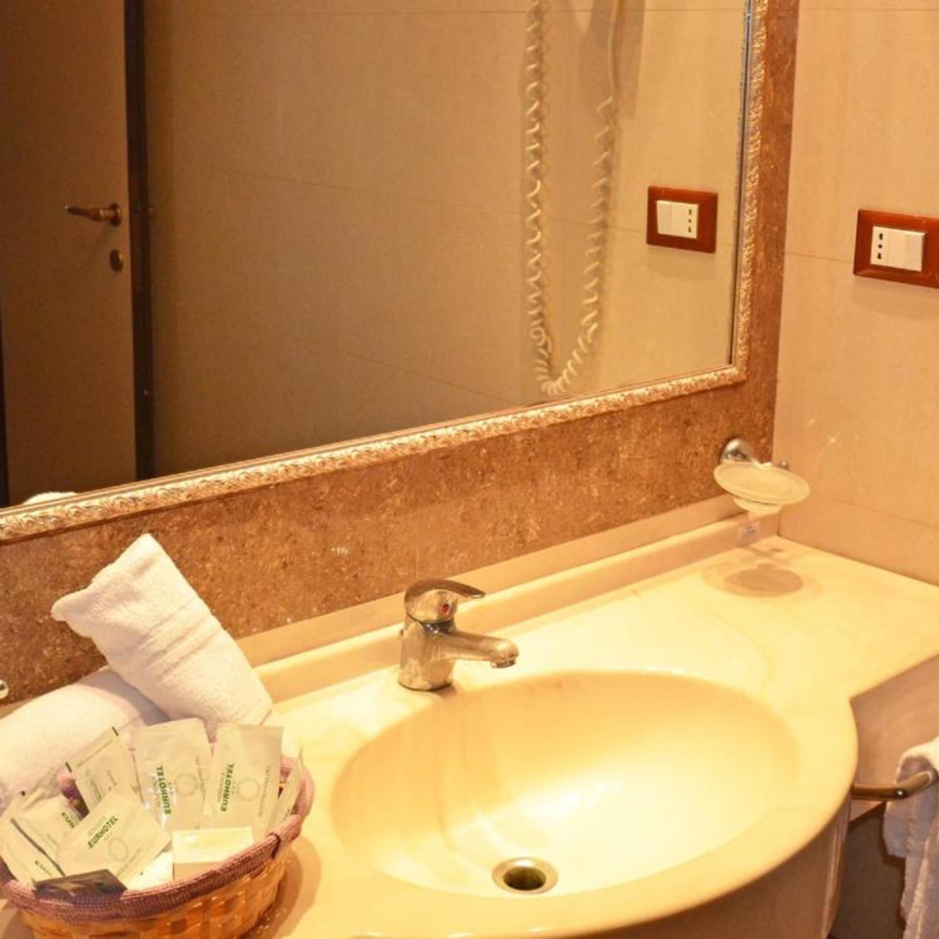 A bathroom with a sink, mirror, and a basket of toiletries.