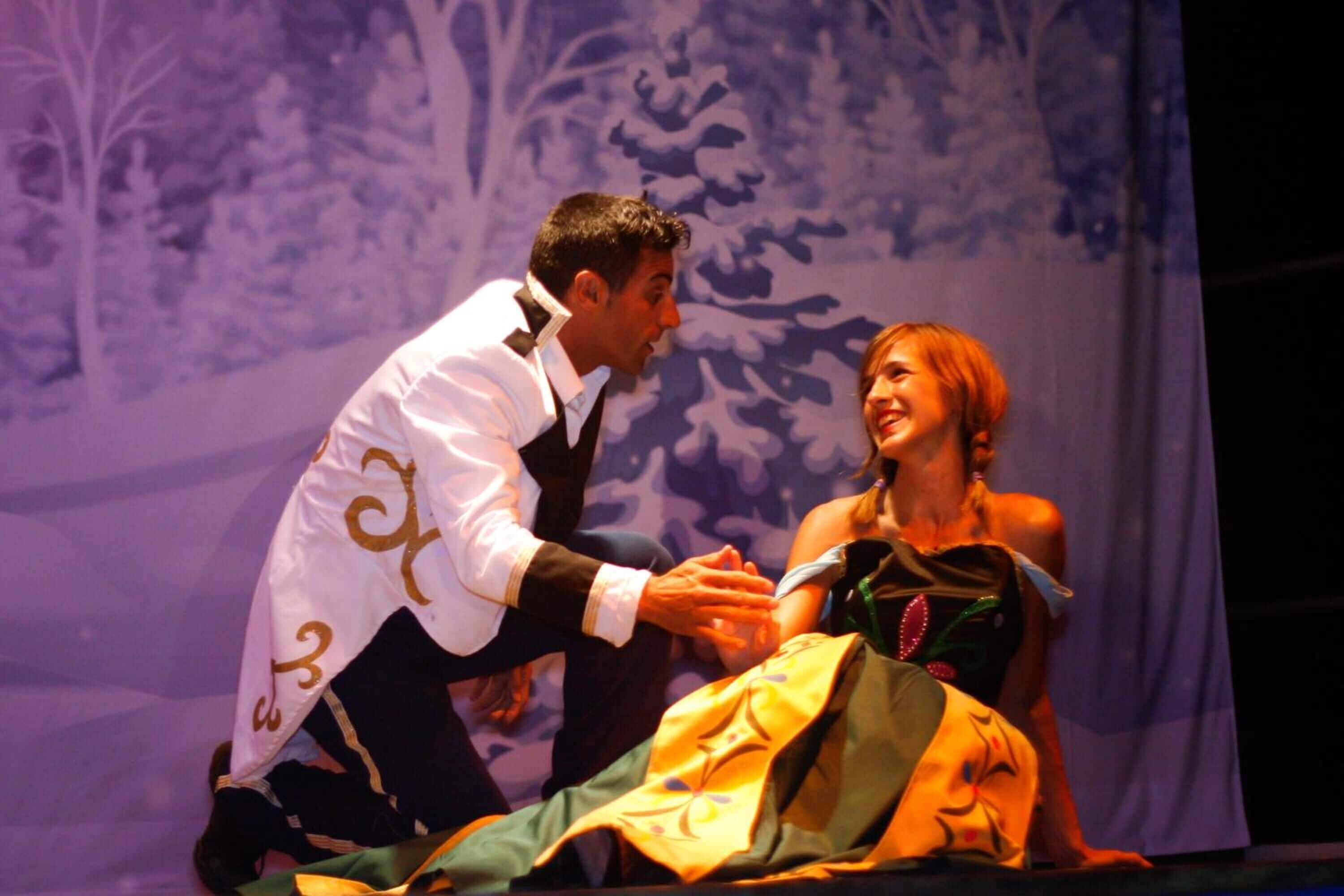 A stage with two people in formal attire, a backdrop with trees, and a curtain.