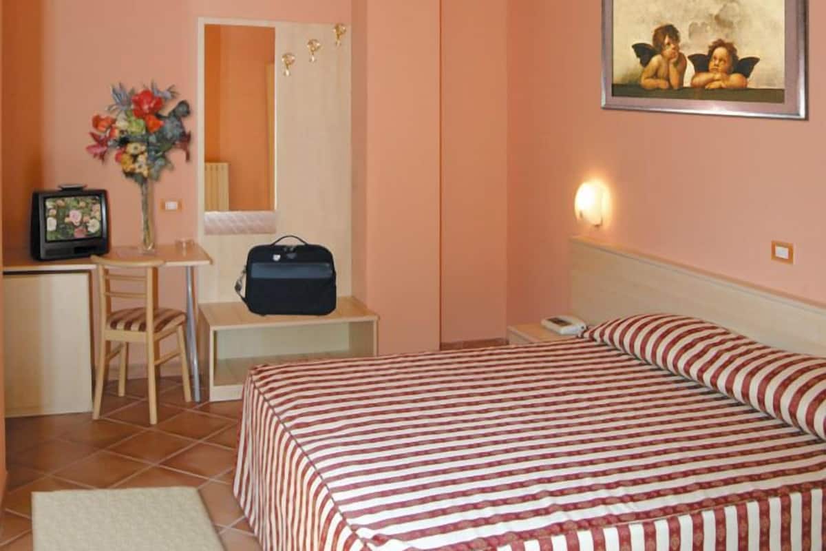 A hotel room with a bed, a desk, a chair, a television, a mirror, and a painting on the wall.