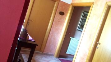 Un pasillo con una puerta de madera, una pequeña mesa con un mantel morado y una decoración de mariposa en la pared.