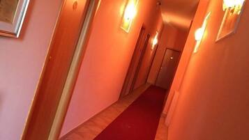 A hallway with a red carpet, wooden doors, and wall-mounted lights.