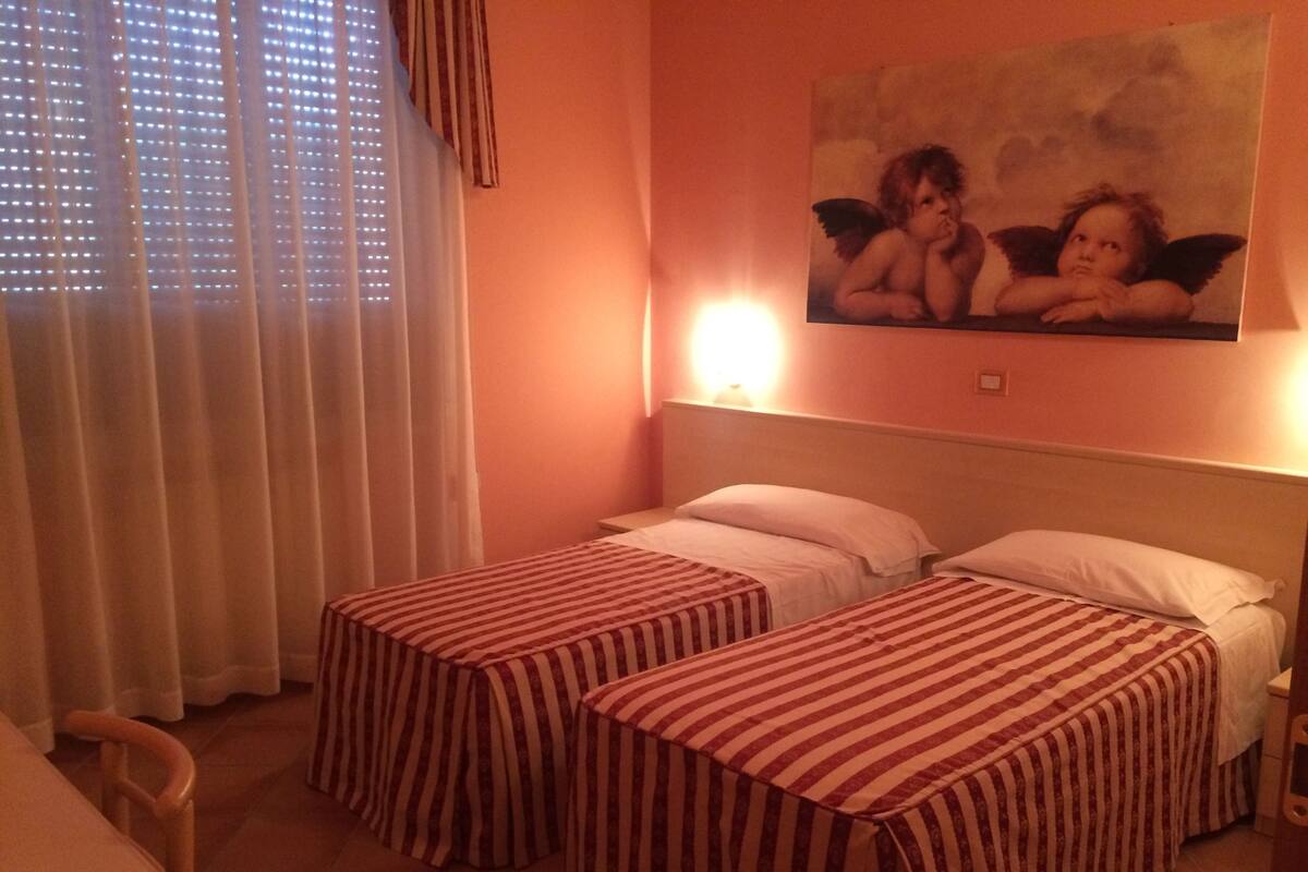 A hotel room with two beds, a table, and a painting on the wall.