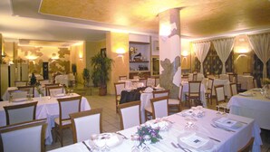 Un restaurante con varias mesas dispuestas para comer, sillas y una planta en maceta.