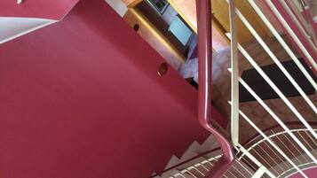 Een trap met een rode leuning en witte spijbels, die uitkomt op een plateau met een deur en een raam.
