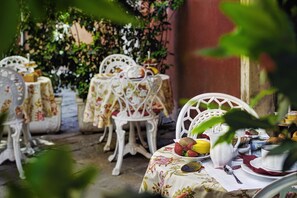 An outdoor dining area with white metal chairs and tables covered with floral tablecloths. - Locanda Fiorita (Venice)