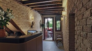A narrow hallway with exposed wooden beams and brick walls, leading to a dining area with a table and chairs. - Locanda Fiorita (Venice)