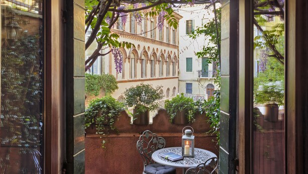 A view of a courtyard with a table and chairs, a lantern, and purple flowering vines. - Locanda Fiorita (Venice)