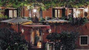 A hotel entrance with a sign, potted plants, and umbrellas. - Locanda Fiorita (Venice)