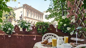 A table set with croissants, juice, and a tiered dessert stand, surrounded by lush greenery and a building with classical architecture in the background. - Locanda Fiorita (Venice)