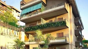 A multi-story residential building with balconies, a paved courtyard, and potted plants.
