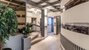 A modern hotel lobby with a staircase, potted plants, and a cityscape mural.