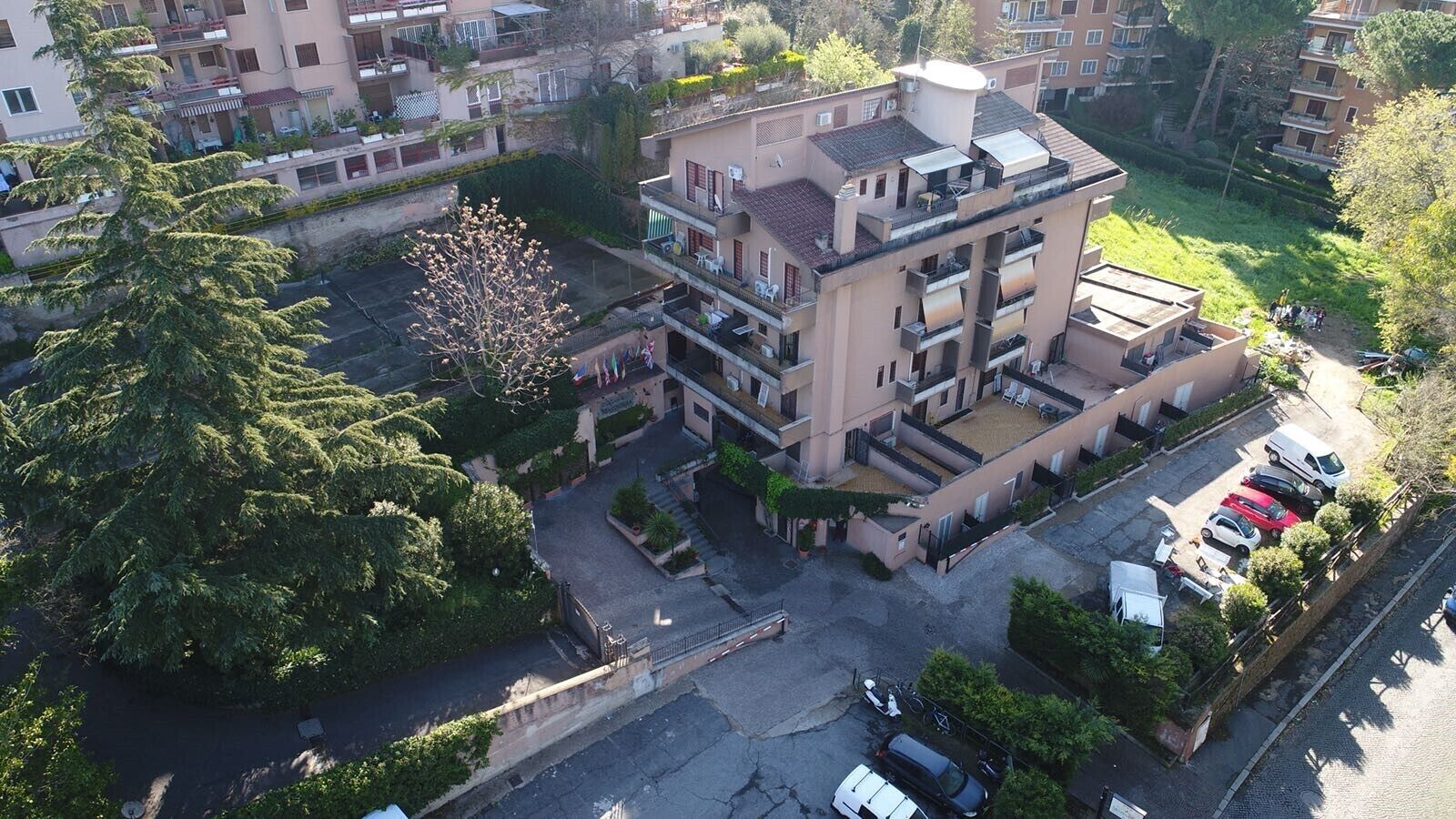 Un edificio residencial de varios pisos con balcones, zona de estacionamiento y zonas verdes aledañas.