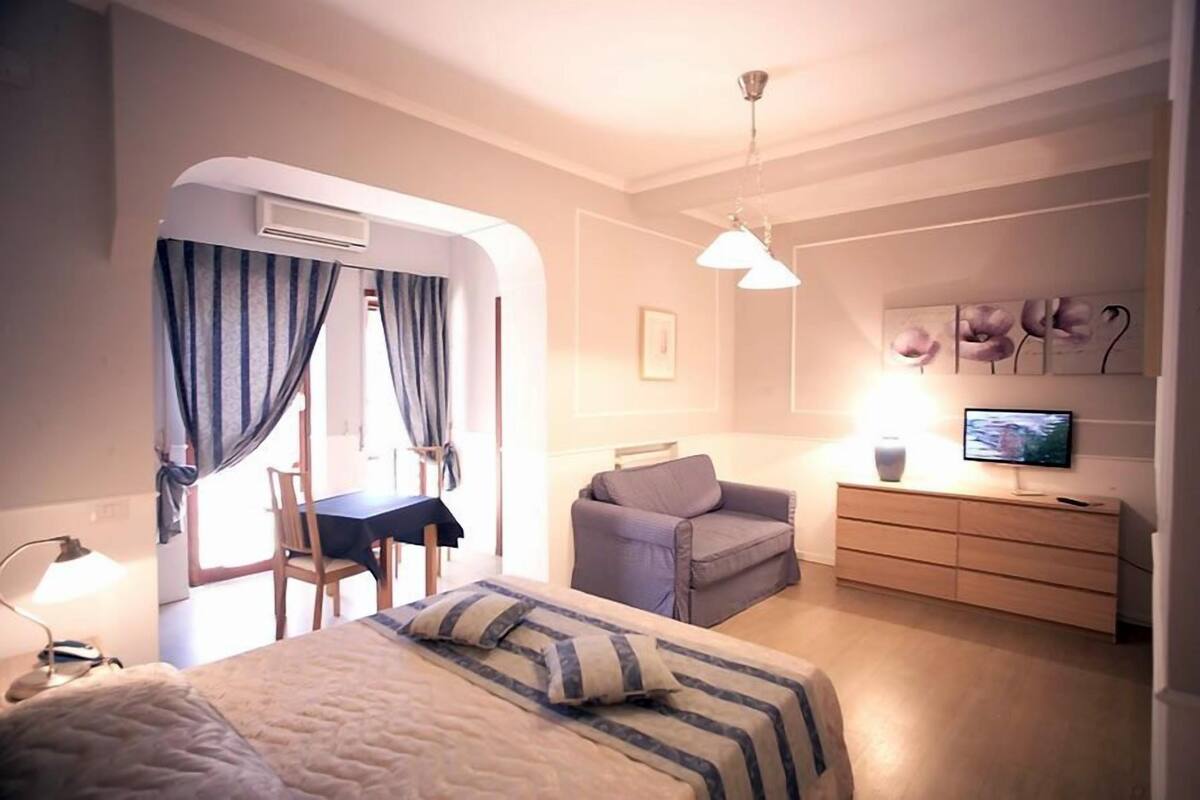 Ein kleines Hotelzimmer mit Bett, Schreibtisch, Stuhl, Sofa, Fernseher und Kommode.