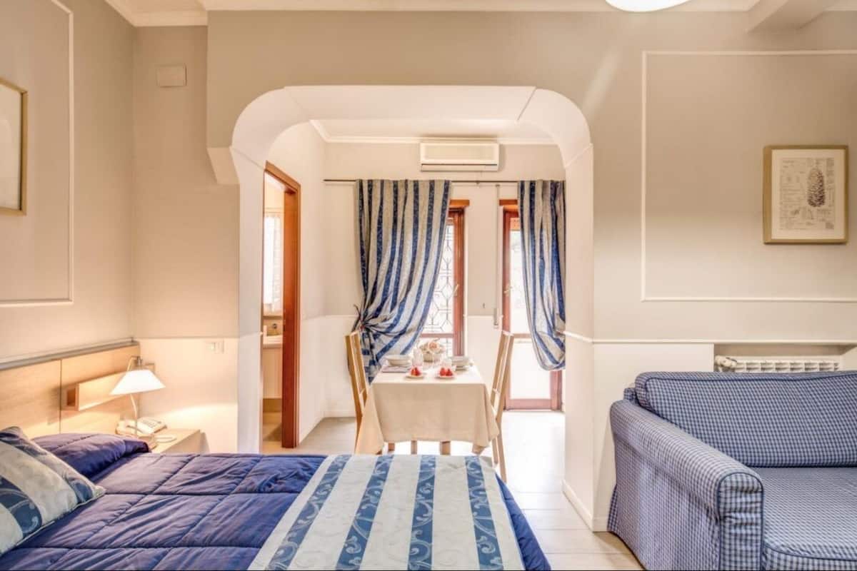Ein Hotelzimmer mit Bett, einer Sitzecke, einem Esstisch und Stühlen sowie Vorhängen.