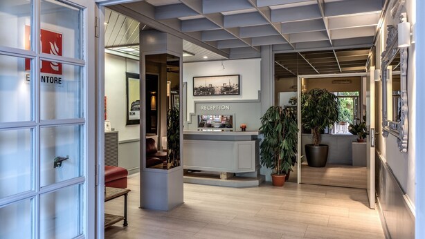 A reception area with a reception desk, a framed cityscape picture, and potted plants.