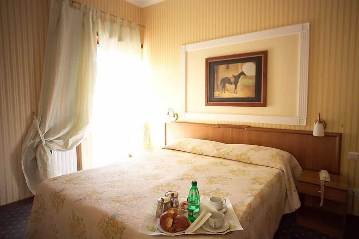 Ein Hotelzimmer mit einem Bett, einem gerahmten Bild an der Wand, einem Nachttisch mit Lampe und einem Tablett mit Frühstücksangeboten.