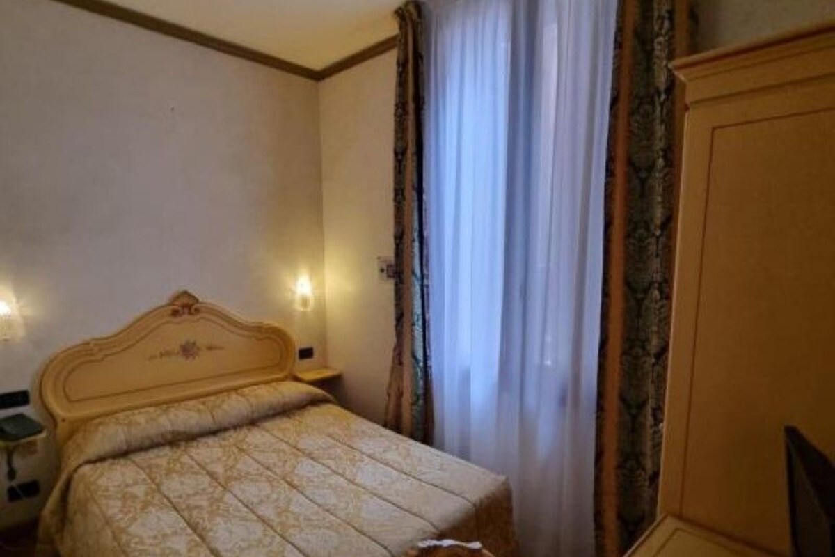 A hotel room with a bed, a desk, a chair, and a wardrobe.