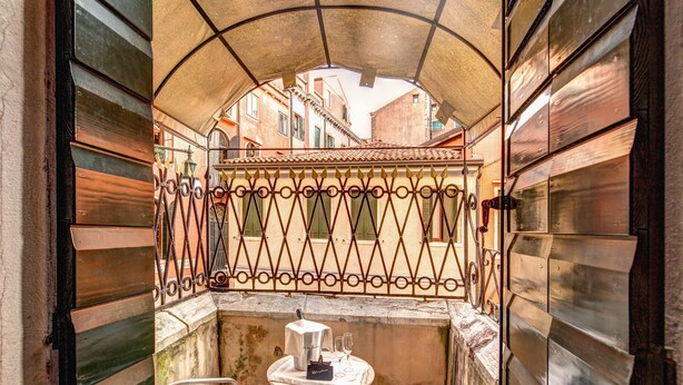 A narrow outdoor balcony with a table and chairs, a metal railing, and a view of buildings in the background. - Residenza Ca' San Marco (Venice)