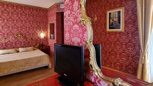 A bedroom with a large ornate mirror, a bed with a white bedspread, and a television on a red dresser. - Residenza Ca' San Marco (Venice)