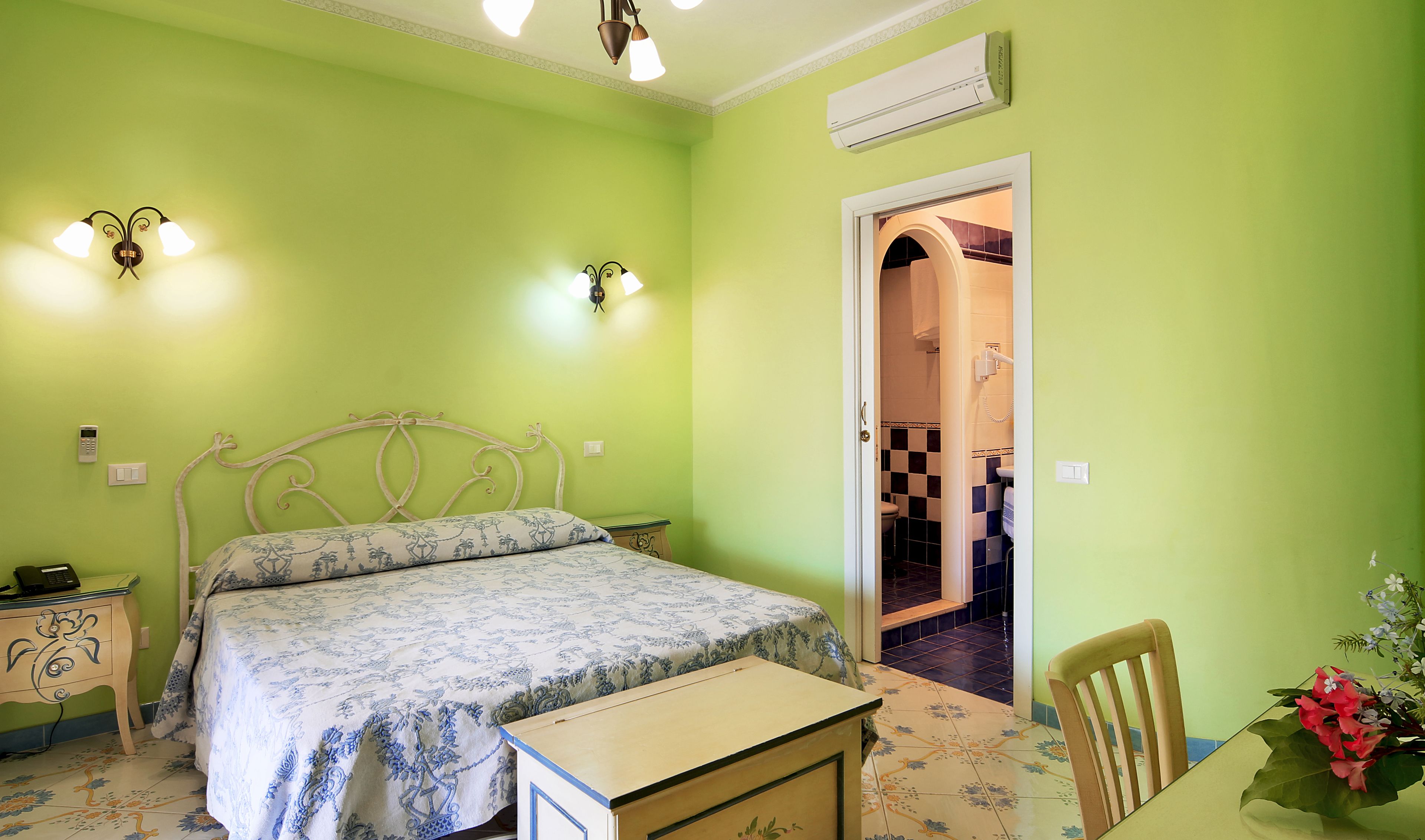 Une chambre à coucher comprenant un lit, des tables de chevet, un bureau, une chaise et une porte donnant sur une salle de bain.