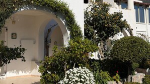 Un bâtiment blanc coiffé d’un toit recouvert de tuiles rouges, doté d’une entrée en arc de cercle et d’un escalier en pierre menant à la porte.