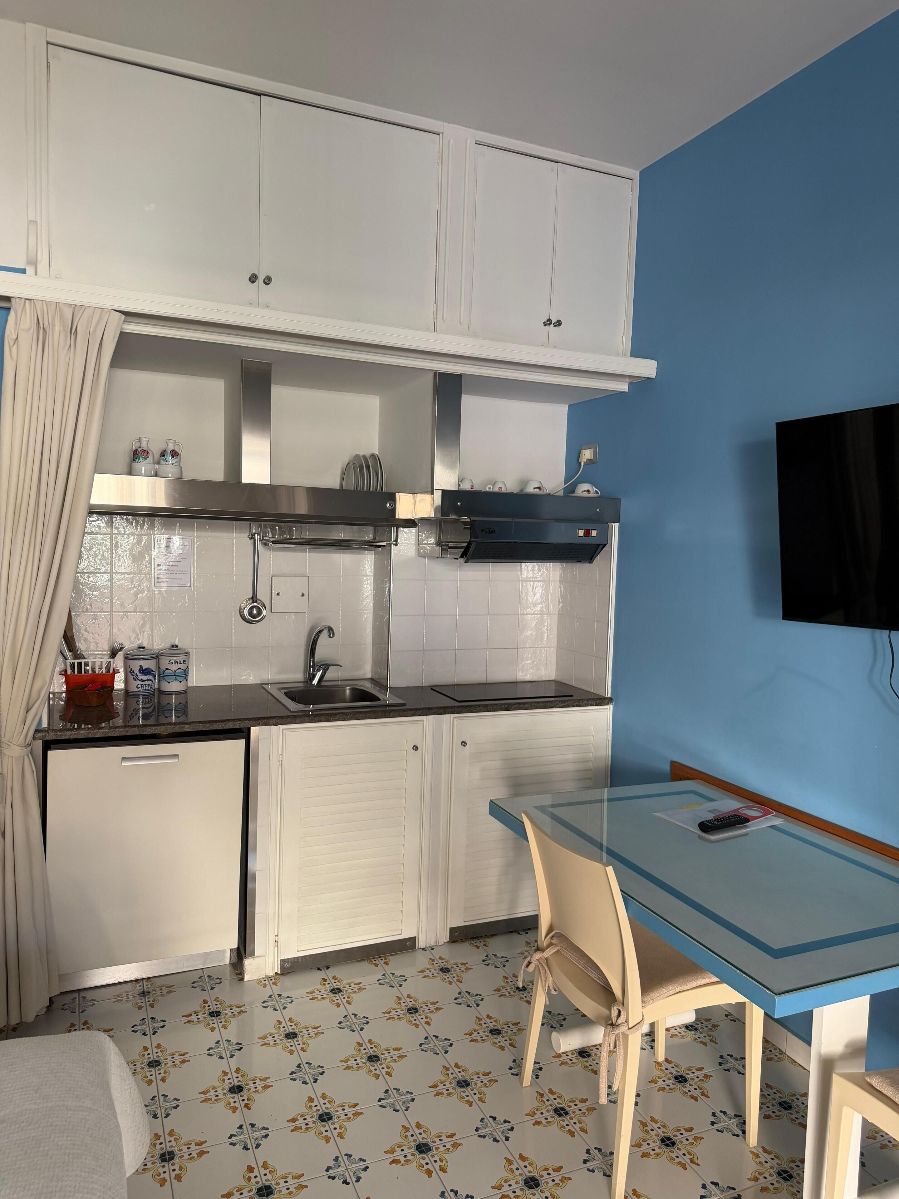 A compact kitchen with a sink, cabinets, a stove, and a small dining area with a table and chair.