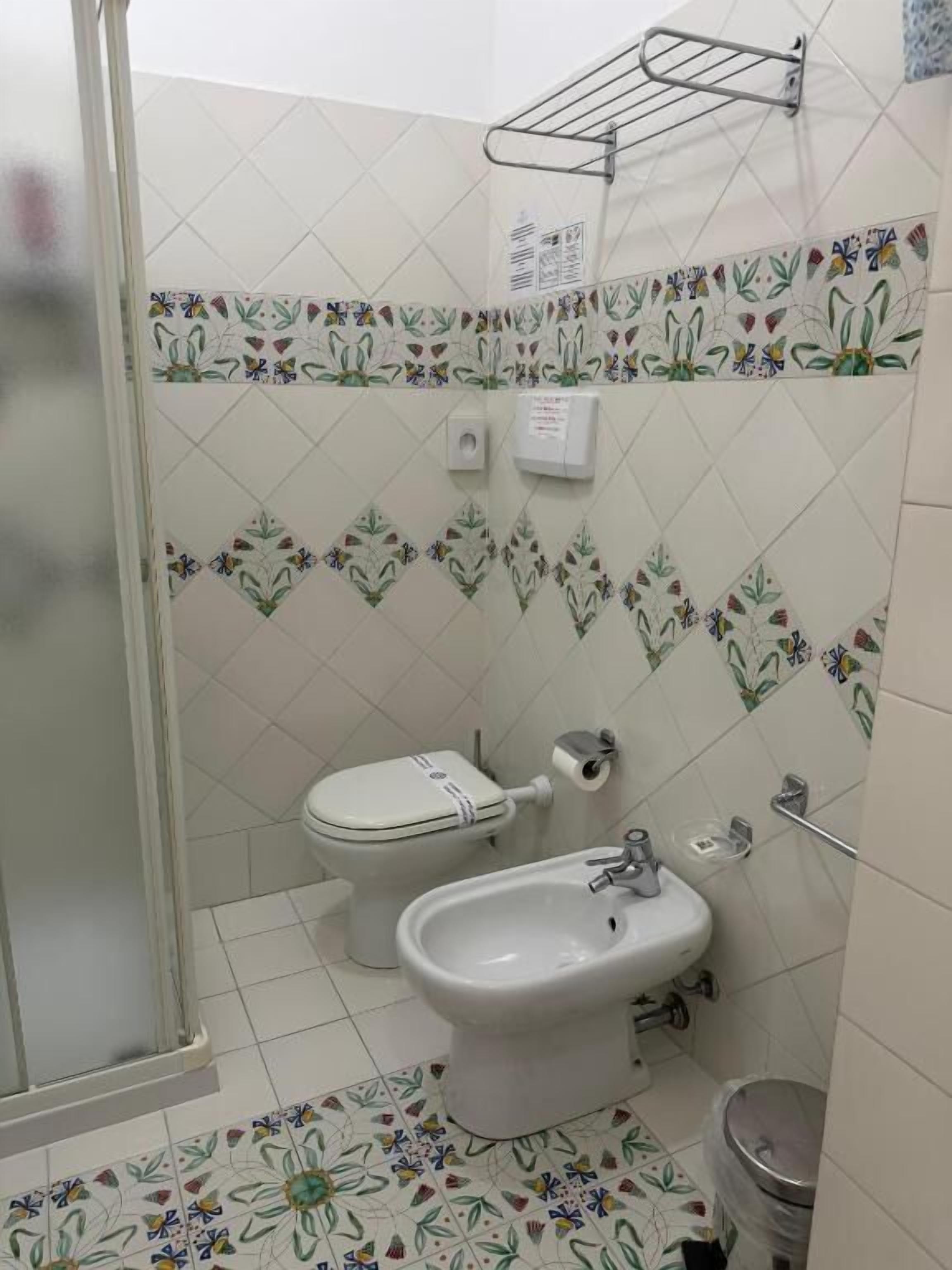 A bathroom with a toilet, bidet, and sink, tiled with floral patterns.