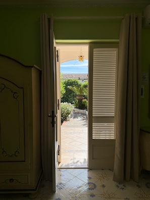 An open door leading to a tiled patio with a view of a building and greenery.