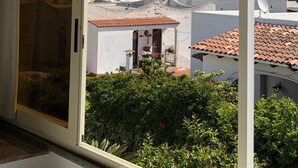 Une vue à travers la fenêtre d’un immeuble doté d’un balcon, d’un mur en pierre et d’une église visible au loin.