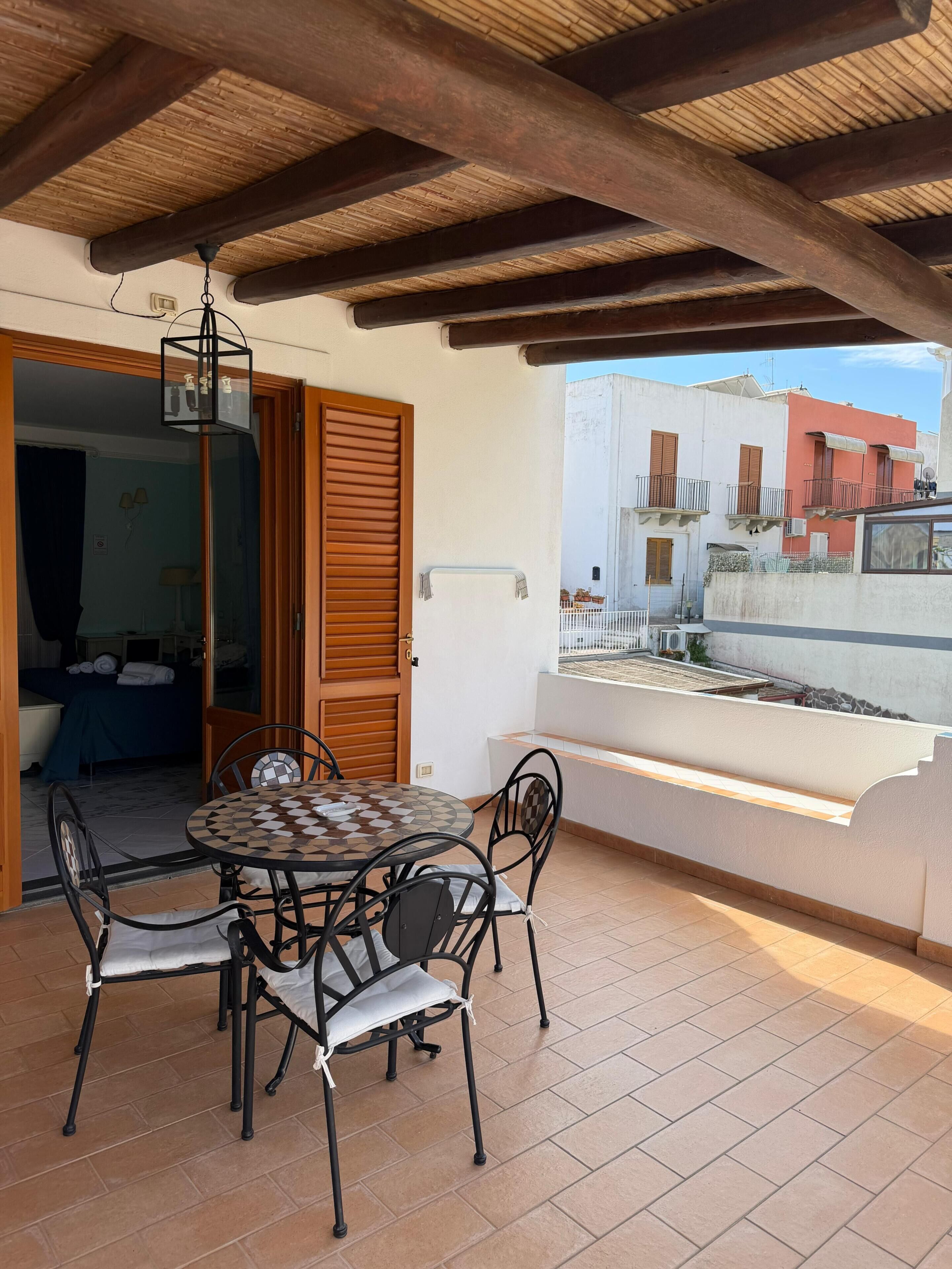 Un patio techado con una mesa y sillas, techo de madera y vistas a edificios cercanos.